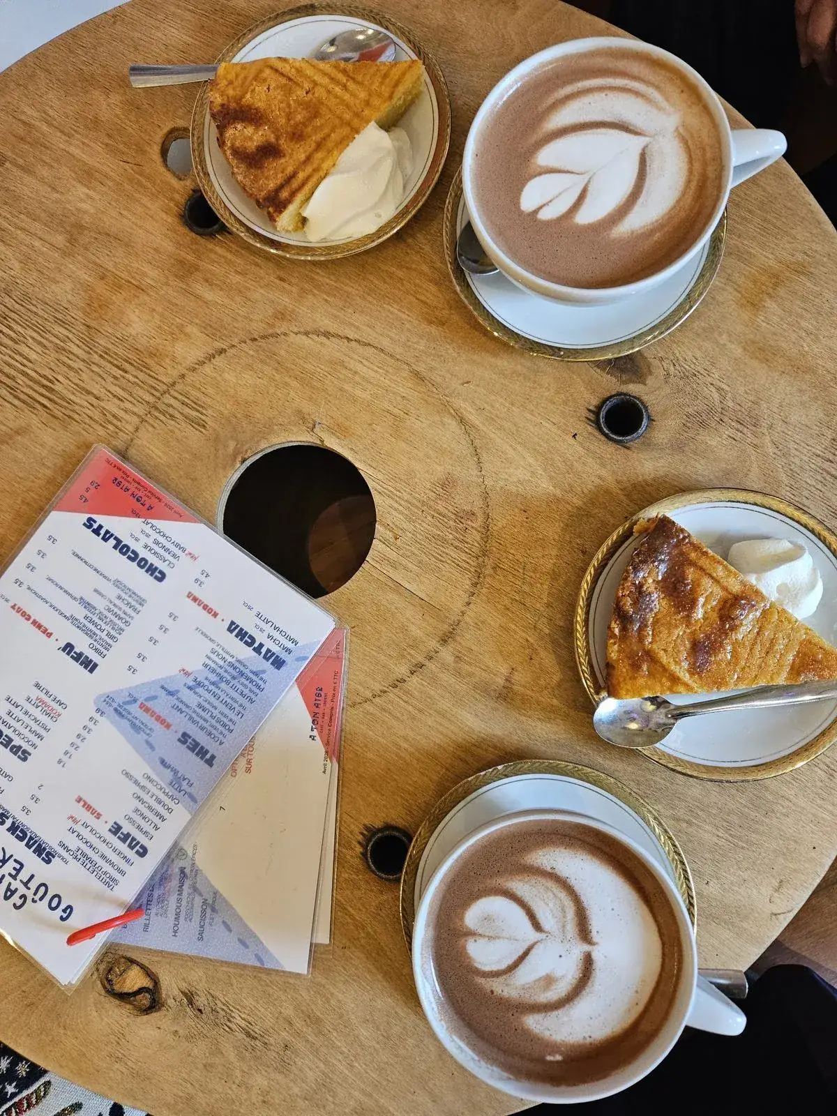 Deux chocolats chauds en latte art et des parts de gâteau sur une table en bois